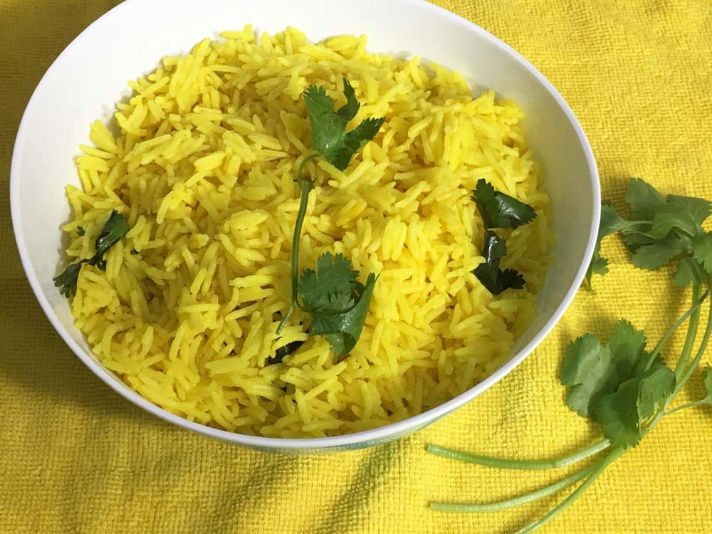 fluffy yellow rice garnished with cilantro leaves served in a bowl