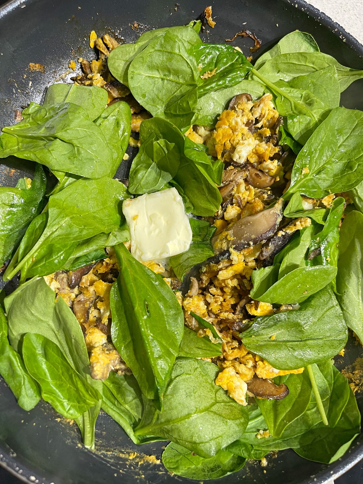 spinach leaves and butter added to mushrooms and eggs